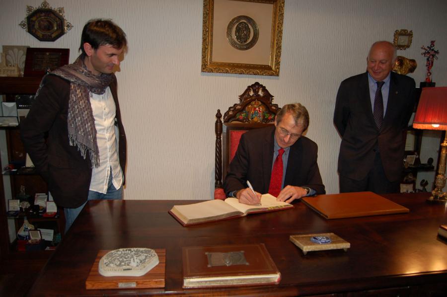 Richard Royce Schrock asinando no libro de honra da USC entre Jorge Mira e o reitor Juan Casares